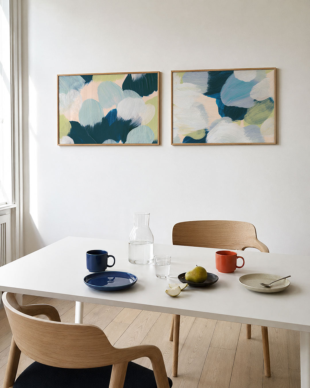 Twee liggende posters met zachte penseelstreken in blauw, groen en wit, aan de muur in een interieur